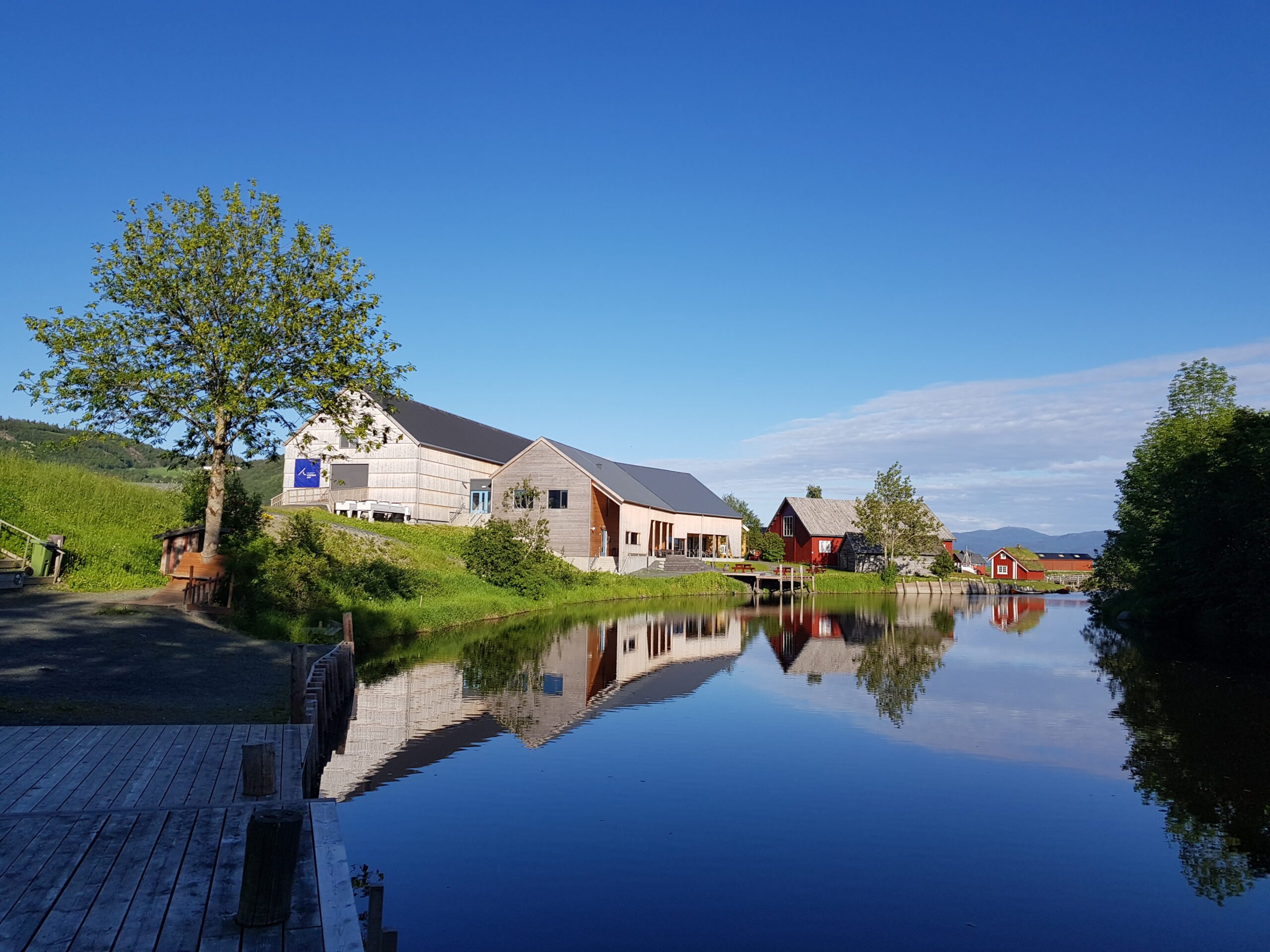 Museet Kystens Arv speiler seg i elva en blå sommerdag