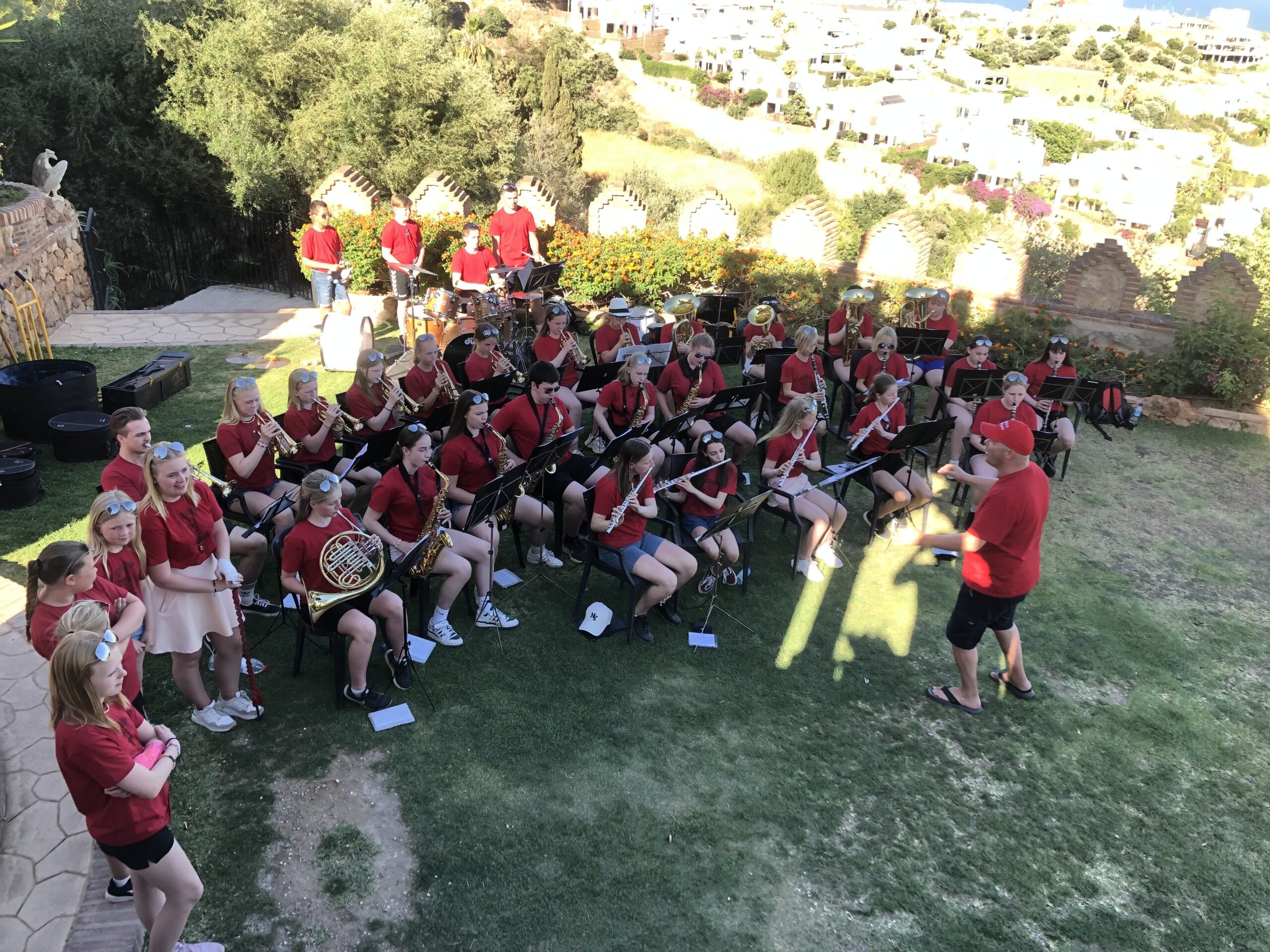 Stadsbygd skolekorps i røde t-skjorter spiller utendørs på tur i Torremolinos
