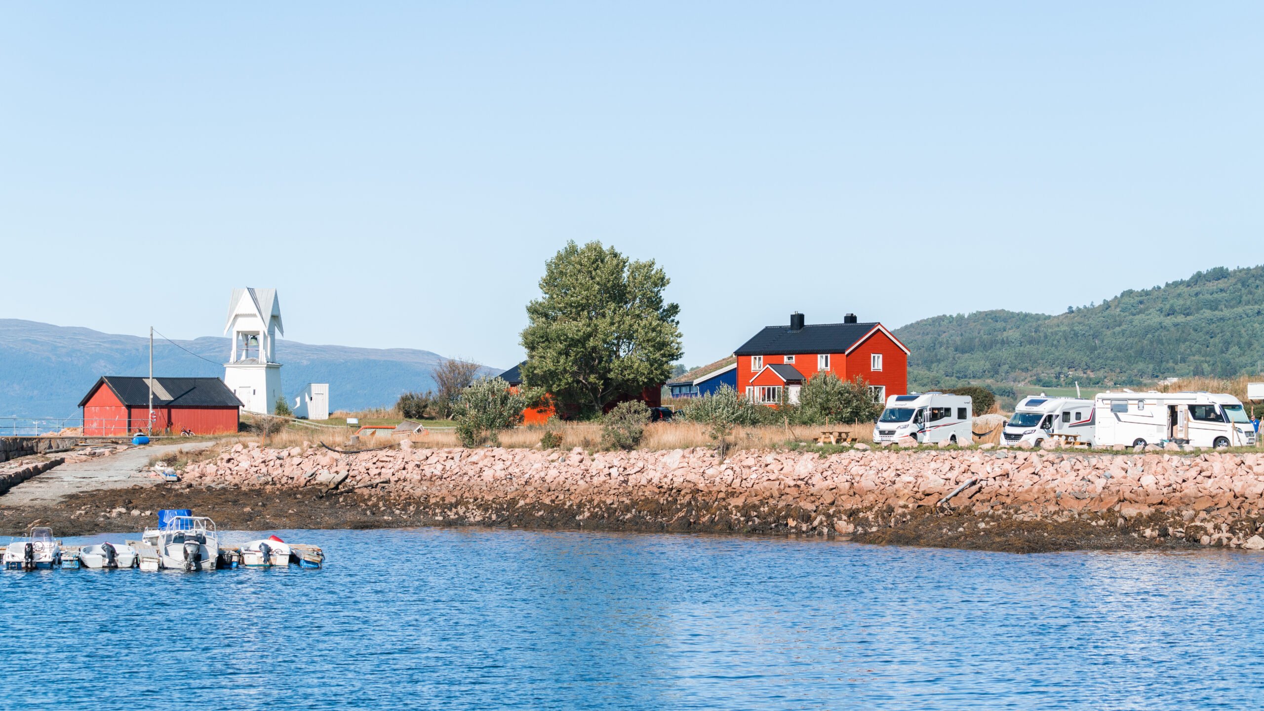 Rødberg sett fra sjøen med klokketårnet, røde hus og bobiler på moloen