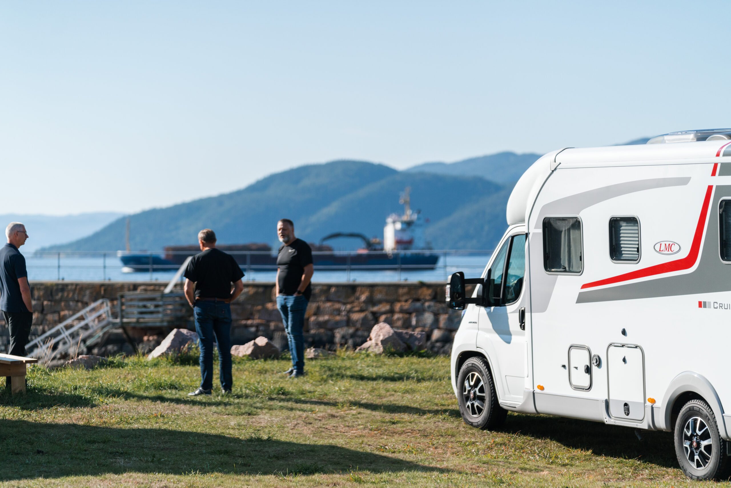 Gjester prater ved en bobil med utsikt over fjorden