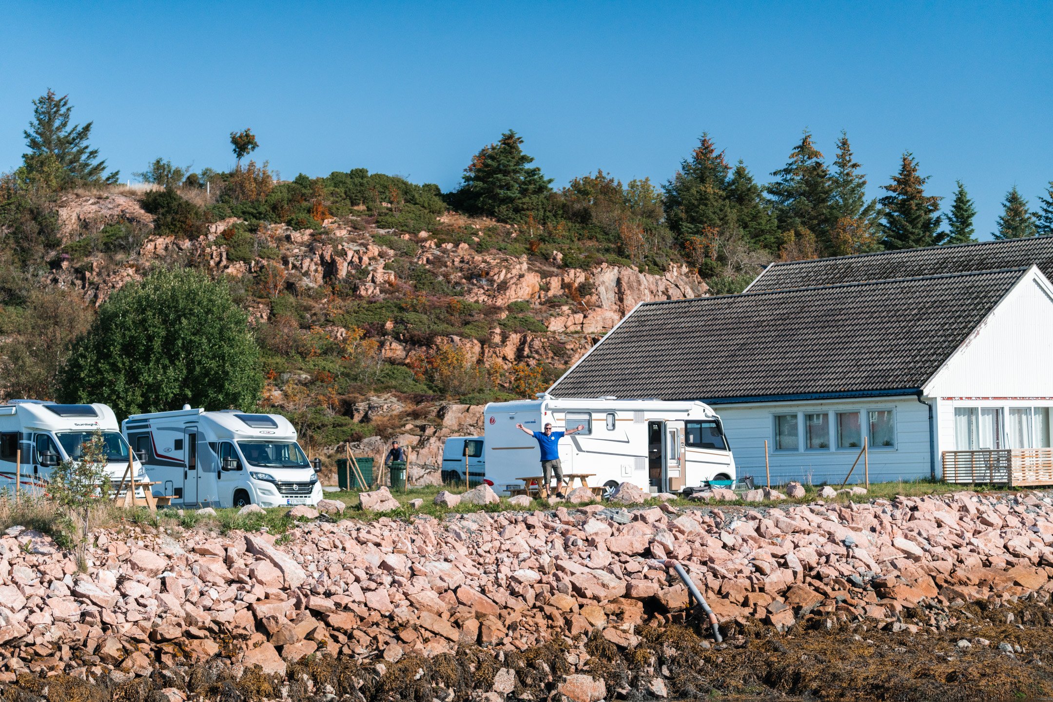 Bobiler parkert ved et hvitt hus i fjæra på Rødberg