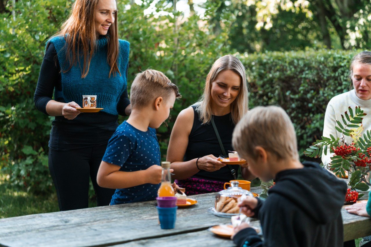 Kvinner og barn koser seg med kaffe og kaker ved et utebord