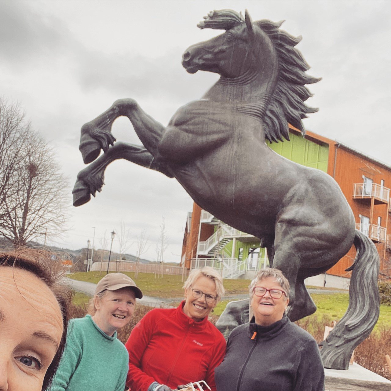 Fire kvinner tar selfie foran en stor hesteskulptur