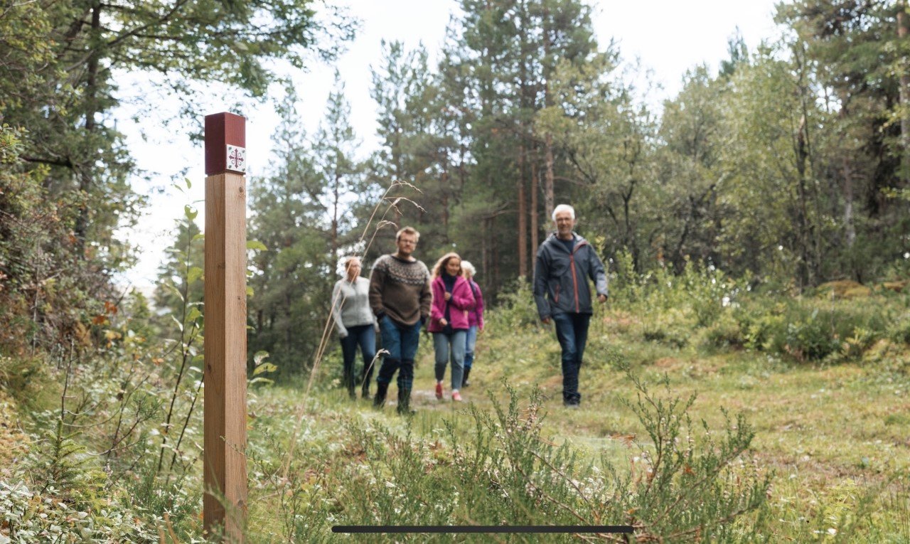 Vandrere på kystpilegrimsleia passerer en pilegrimsstolpe i skogen